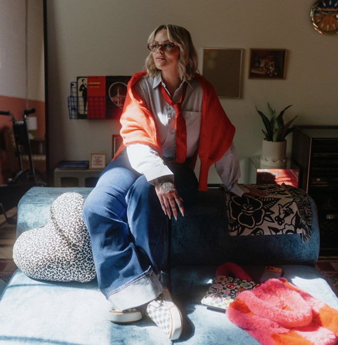 Heather sitting on a blue sofa in a red sweater & glasses