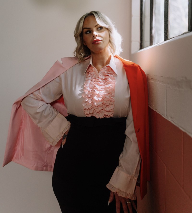 Heather standing beside a window in a pink blouse & jacket