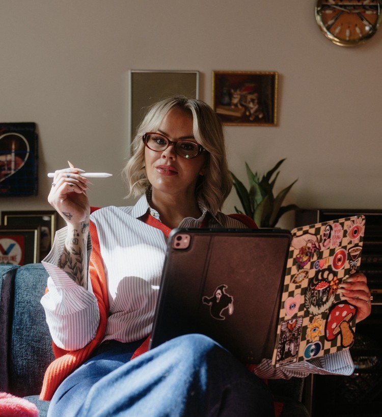 Heather sitting on a sofa with her tablet & notebook