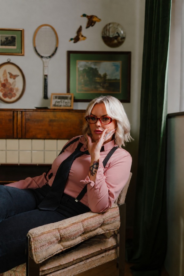 Heather seated in a chair wearing red glasses and a pink blouse